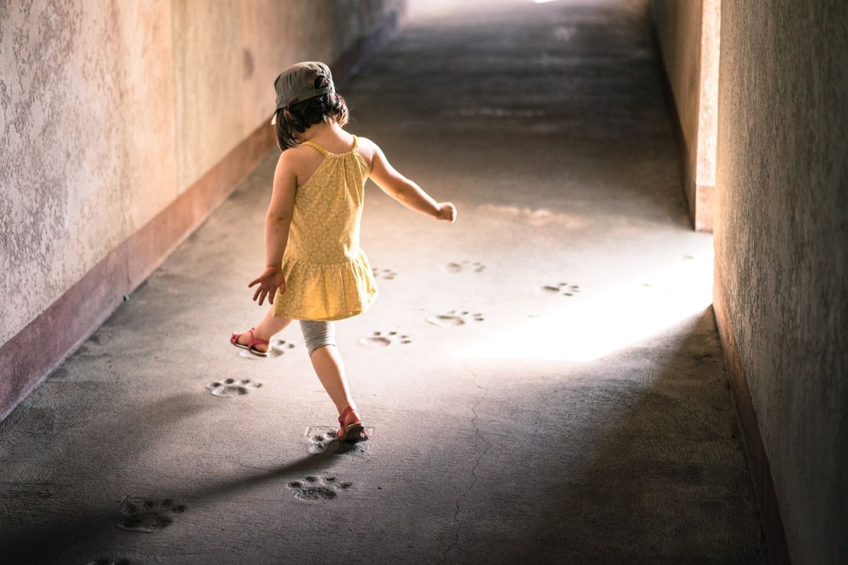 A small girl wearing yellow dress walking over cat marks in cement